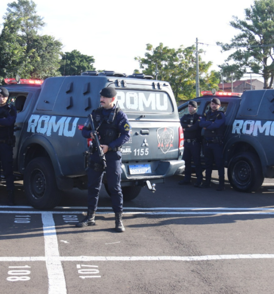 Group of tactical police officers standing in front of two large armored vans marked ROMU in a parking lot