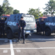 Group of tactical police officers standing in front of two large armored vans marked ROMU in a parking lot