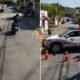 Urban street police checkpoint a Polícia Militar officer on foot and a motorcyclist stopped ahead with a patrol car blocking the road and traffic cones lined up