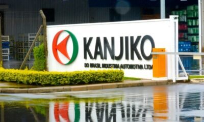 Industrial facility entrance with a white sign reading KANJIKO and a red green circular logo wet pavement reflects the sign