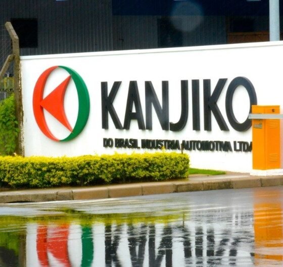 Industrial facility entrance with a white sign reading KANJIKO and a red green circular logo wet pavement reflects the sign