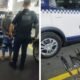 Uniformed officer escorts a handcuffed man toward a GCM police van in a parking area with equipment nearby