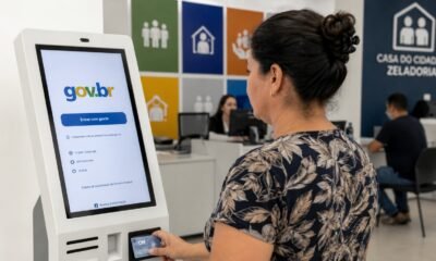 Woman using a govbr self service kiosk at a counter in a government office card in hand intake screen visible