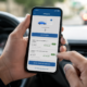 Pessoa no carro segura o celular exibindo um app de infrações de trânsito com o total de  infrações na tela