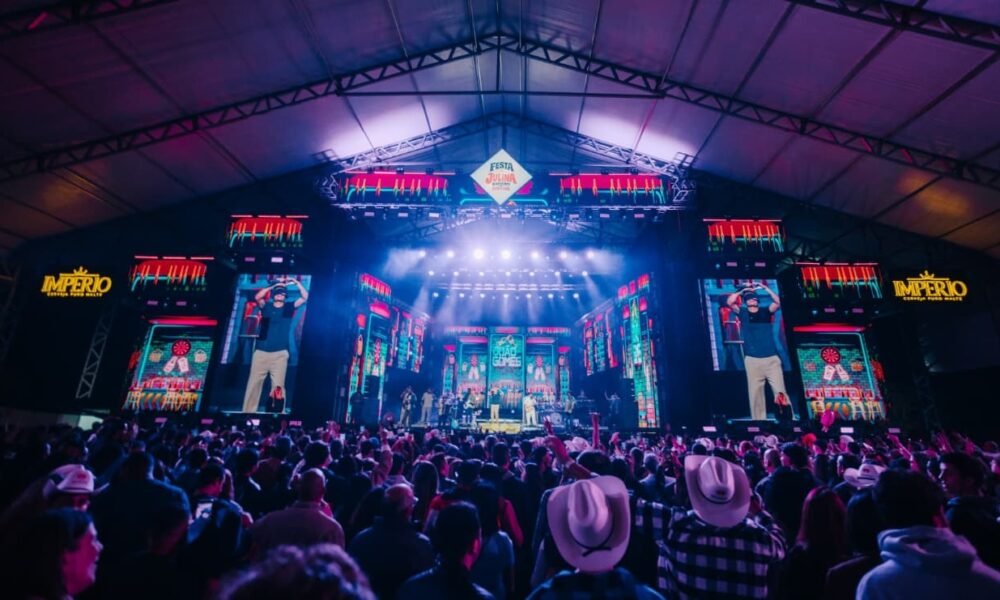 Large indoor concert stage with bright neon lights and a crowd facing the performers under a peaked roof festival tent