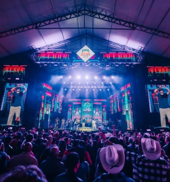 Large indoor concert stage with bright neon lights and a crowd facing the performers under a peaked roof festival tent