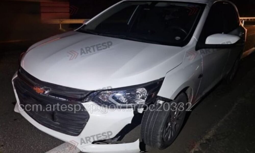 White Chevrolet sedan at night with front bumper damaged and hanging, parked on a dark road edge