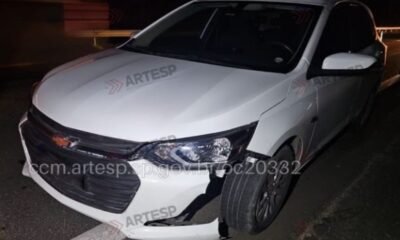 White Chevrolet sedan at night with front bumper damaged and hanging parked on a dark road edge