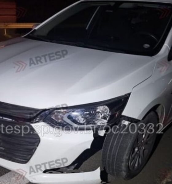 White Chevrolet sedan at night with front bumper damaged and hanging parked on a dark road edge