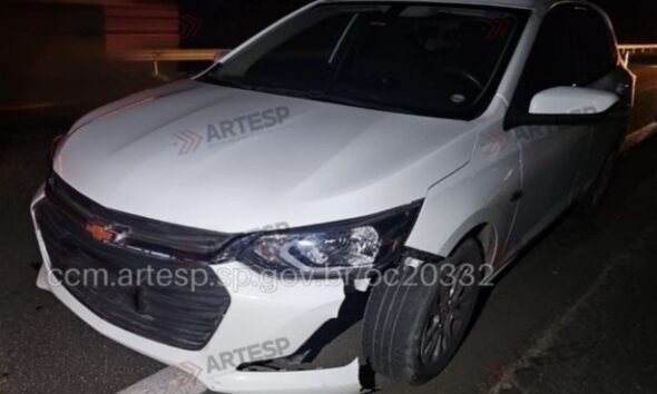 White Chevrolet sedan at night with front bumper damaged and hanging parked on a dark road edge