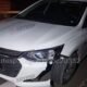 White Chevrolet sedan at night with front bumper damaged and hanging parked on a dark road edge