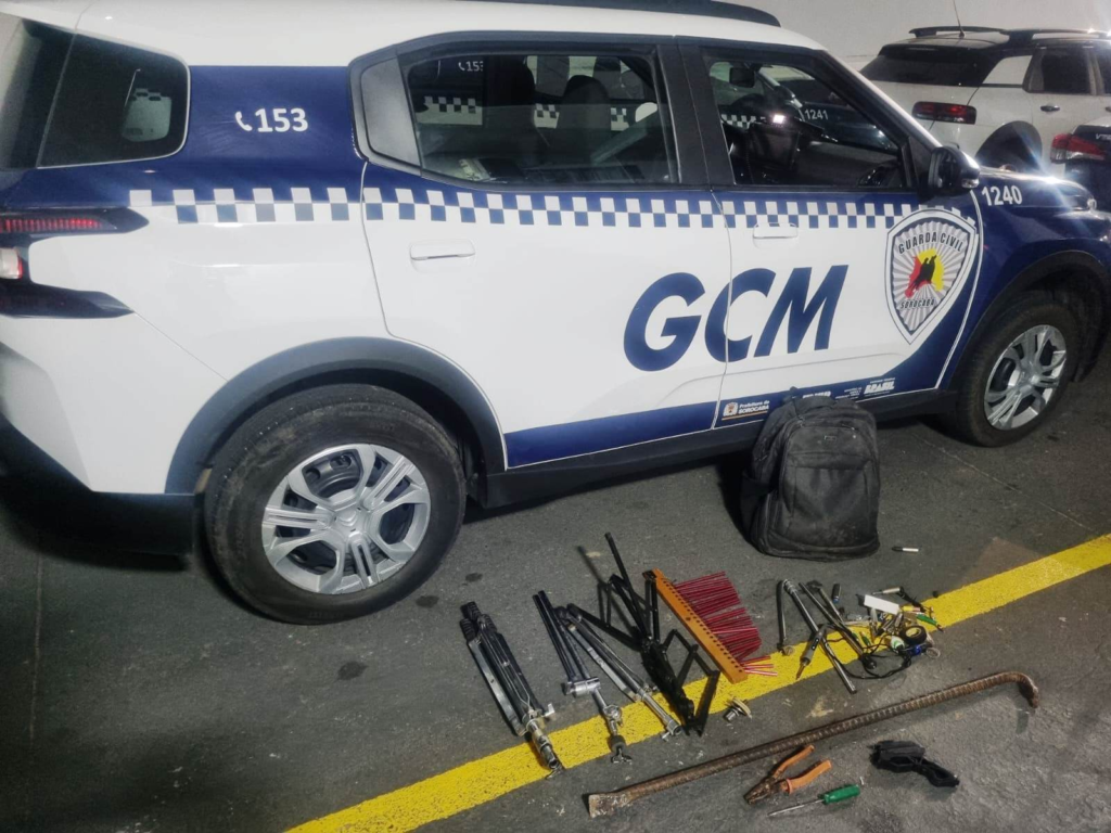 Blue and white patrol SUV with GCM emblem parked in a lot various hand tools and a backpack laid out on the ground in front of it