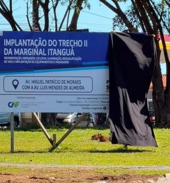 Billboard advertising a roadworks project in Portuguese mounted on a metal frame with a black cloth covering the right side