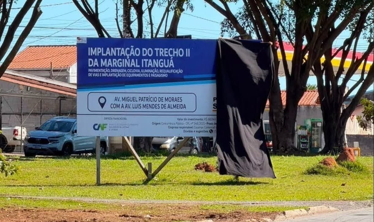 Billboard advertising a roadworks project in Portuguese mounted on a metal frame with a black cloth covering the right side