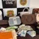 Seized collection of luxury handbags wallets and cash laid out on a table by Polícia Civil São Paulo backdrop
