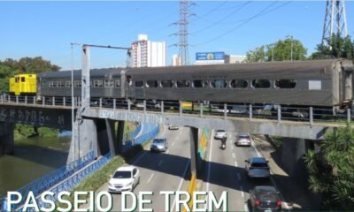 Passenger train on an elevated bridge crossing a busy road with cars driving beneath and city buildings in the background