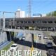 Passenger train on an elevated bridge crossing a busy road with cars driving beneath and city buildings in the background
