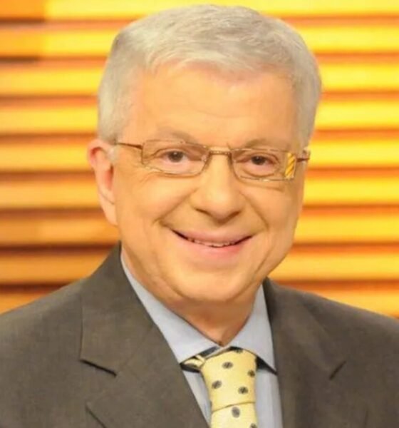 Smiling middle aged man in a gray suit and yellow polka dotted tie wearing glasses against a warm wooden slat background