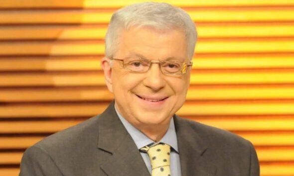 Smiling middle aged man in a gray suit and yellow polka dotted tie wearing glasses against a warm wooden slat background
