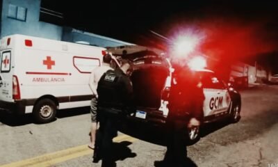 Nighttime emergency scene with an ambulance and a GCM police vehicle responders near the open trunk with red flashing lights in the background