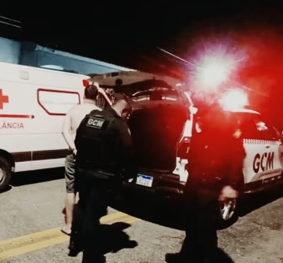Nighttime emergency scene with an ambulance and a GCM police vehicle responders near the open trunk with red flashing lights in the background