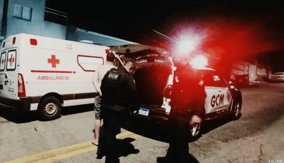 Nighttime emergency scene with an ambulance and a GCM police vehicle responders near the open trunk with red flashing lights in the background