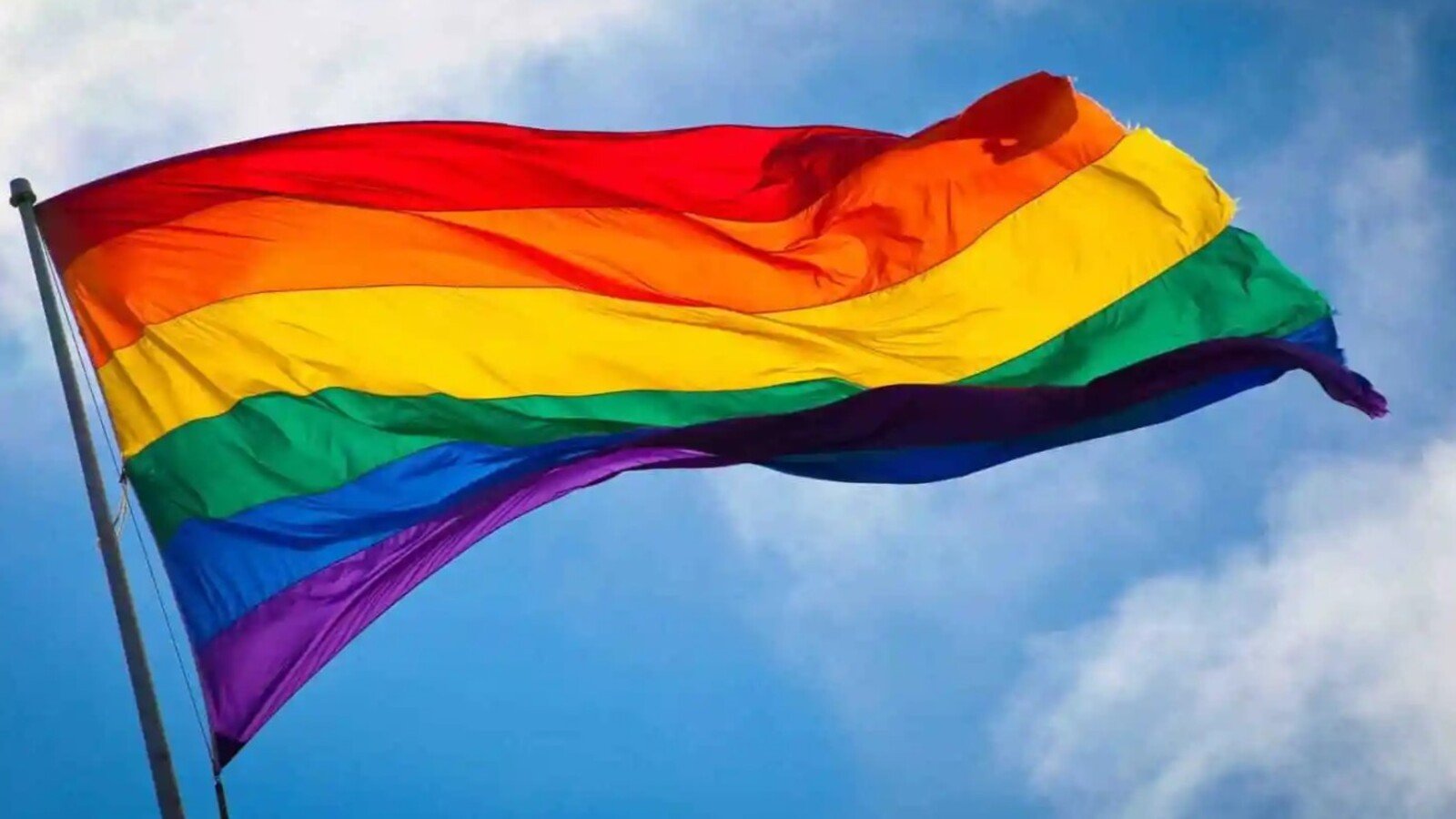 Rainbow Pride flag waving against a blue sky symbolizing LGBTQ pride and diversity