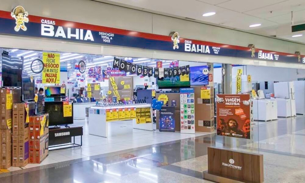 Bright electronics store inside a mall, with stacked boxes, yellow sale signs, and checkout counters in the background.