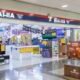 Bright electronics store inside a mall with stacked boxes yellow sale signs and checkout counters in the background