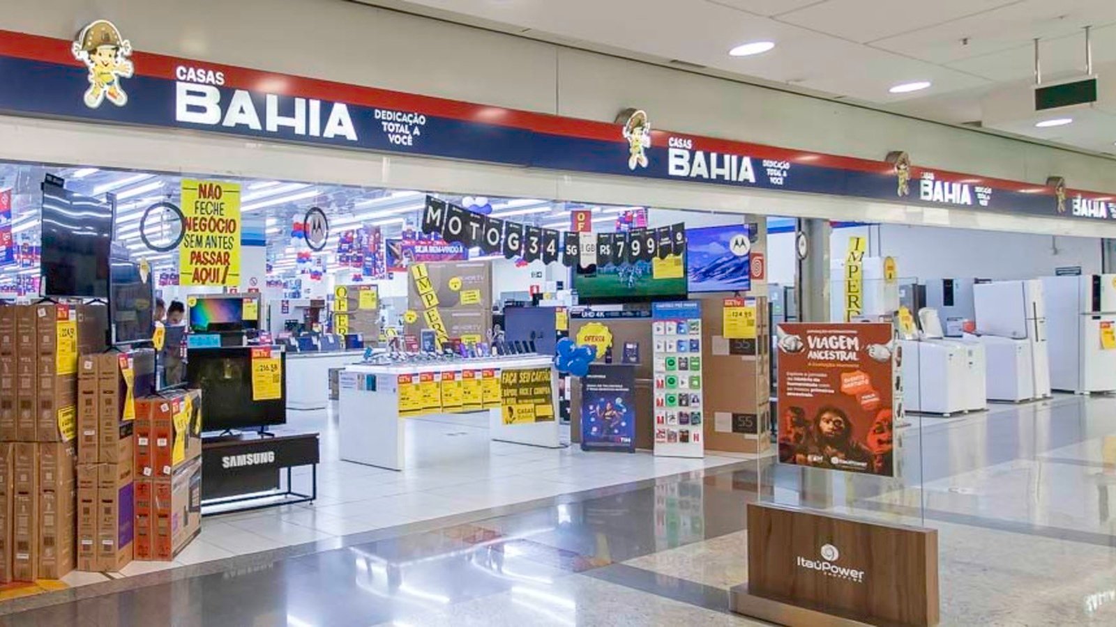 Bright electronics store inside a mall with stacked boxes yellow sale signs and checkout counters in the background
