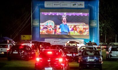 Drive-in cinema at night with a large blue inflatable screen frame and a big cartoon movie on screen, cars lined up in front watching the show.
