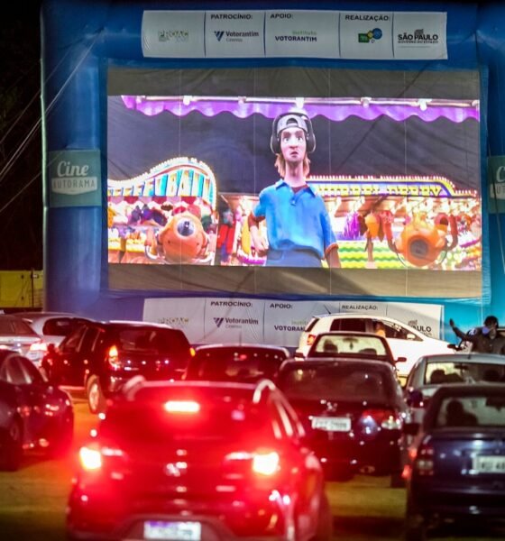 Drive in cinema at night with a large blue inflatable screen frame and a big cartoon movie on screen cars lined up in front watching the show