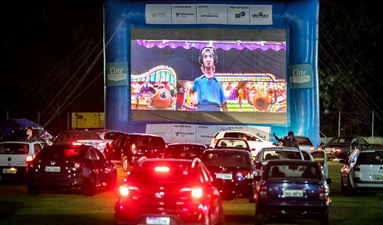 Drive in cinema at night with a large blue inflatable screen frame and a big cartoon movie on screen cars lined up in front watching the show