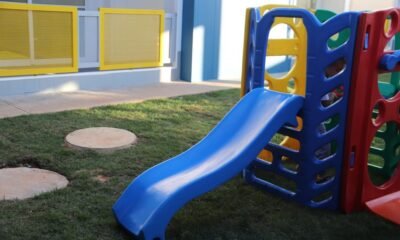 Blue plastic slide connected to a multicolored play structure on a grassy outdoor area.
