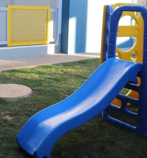 Blue plastic slide connected to a multicolored play structure on a grassy outdoor area