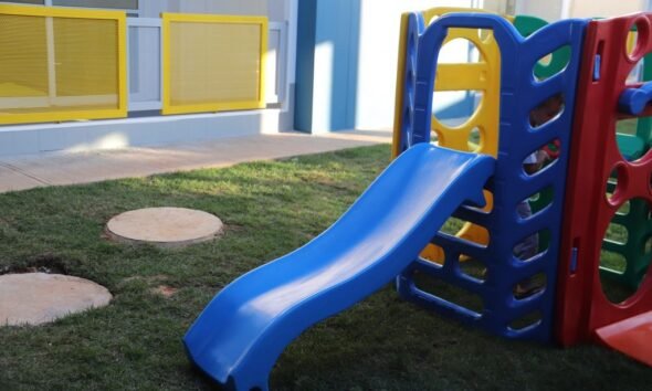 Blue plastic slide connected to a multicolored play structure on a grassy outdoor area