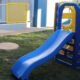 Blue plastic slide connected to a multicolored play structure on a grassy outdoor area